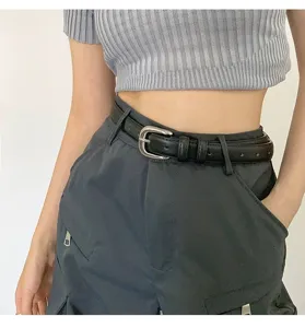 Detail close-up of a stylish black leather belt with a sleek silver buckle on trousers.
