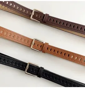 Detail shot of perforated leather belts in three colors with silver metal pin buckles.