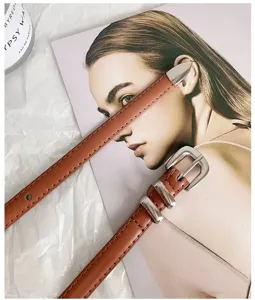 Detailed shot of brown thin leather belt with silver metal buckle on editorial background.