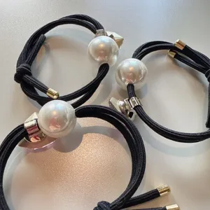 Vue détaillée de l'élastique à cheveux noir avec grosse perle et décoration triangle en cristal.