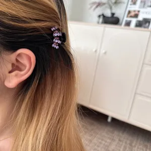 Close-up detail of a small rhinestone hair claw clip featuring purple and pink crystals.