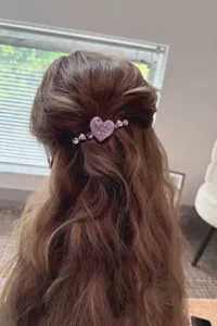 Detail shot showing a purple rhinestone heart hair clip worn on half-up wavy brown hair.