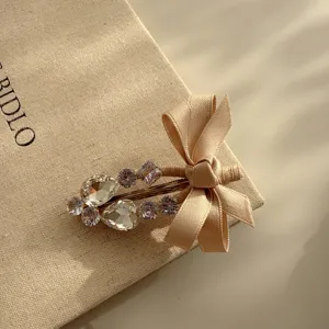 Detail shot of a sweet rhinestone bow hair clip, elegant beige fabric accessory for women.