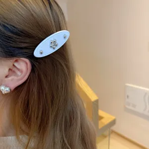 Close-up detail of white acetate hair clip with metallic bead flower design worn on hair.