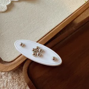 Close-up of white oval hair barrette with silver bead flower and metal dots detail.