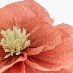 Handmade crepe paper flower detail shot, peach pink petals and yellow stamen texture.