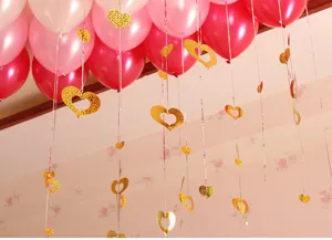 Detailed shot of hanging golden glitter heart pendants and colorful balloons for party decor.