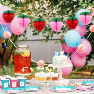 Detail view of colorful strawberry honeycomb balls hanging in a festive outdoor party setting.