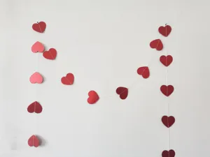 Detail shot of red and pink heart paper garland hanging on wall for party decor scene.