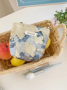 Embossed floral makeup bag detail shot, stylish blue and yellow fabric cosmetic storage pouch.