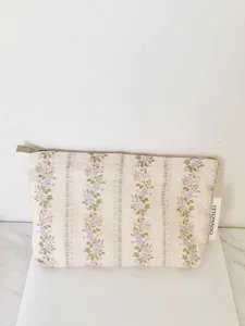 Vintage floral cosmetic pouch detail showing delicate purple stripe pattern and metal zipper closure.