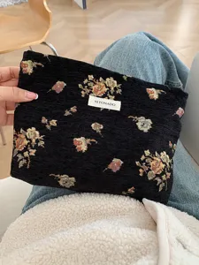 Detail view of the vintage floral tapestry cosmetic pouch held in hand, showing fine woven texture.