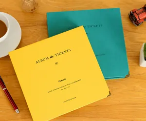 Detailed view of colorful ticket storage albums with metal corner protectors on a wooden table.