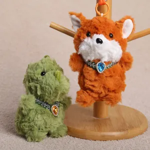 Detailansicht von Plüschtier-Anhängern mit niedlichem Fuchs und Dinosaurier sowie Strass-Halsbändern.