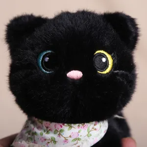 Gros plan détaillé du pendentif chat en peluche noire avec yeux bicolores et foulard.