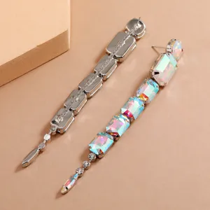 Close-up view of long silver dangle earrings featuring multicolored iridescent crystal stones.