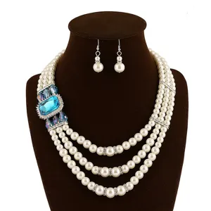 Detailopname van de meerlaagse parelketting met een groot blauw kristal en bijpassende oorbellen.