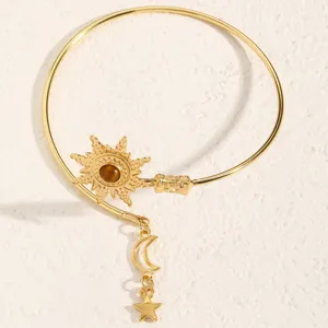 Primo piano di bracciale aperto dorato con motivo sole, pietra marrone e ciondoli luna e stella.