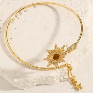 Dettaglio bracciale rigido aperto in metallo dorato con motivo sole e ciondoli raffinati.