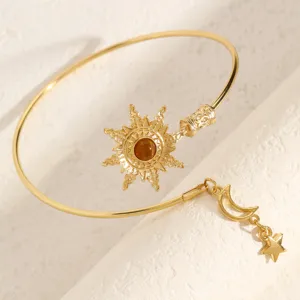 Dettaglio di un bracciale rigido dorato con ciondolo sole e pendente stella e luna.