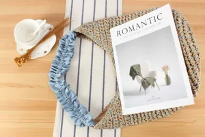 Détail du sac porté épaule tissé, bandoulière froncée bleue et paille sur bois.