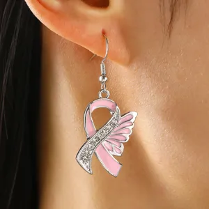 Detailed close-up view of the pink ribbon angel wings crystal rhinestone dangle earrings worn.