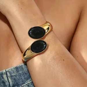 Detailed close-up view of the gold-tone open cuff bracelet featuring dual oval black stones.
