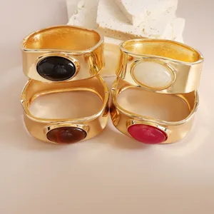 Gold wide cuff bracelet set with oval colored stones, statement metal jewelry details.