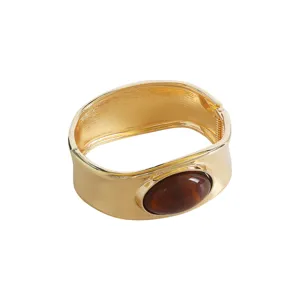 Elegant wide gold-tone hinged bangle bracelet featuring a classic oval brown stone centerpiece.