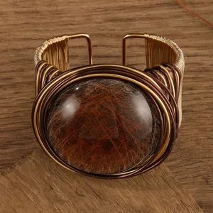 Primo piano dettagliato del bracciale rigido largo con filo e grande gemma in resina marrone.