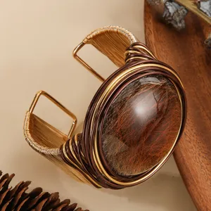 Dettaglio di un bracciale rigido largo con intreccio in filo di alluminio e gemma in resina.