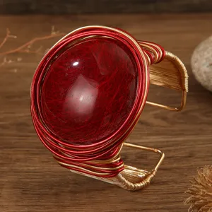 Primo piano dettagliato del bracciale rigido aperto con grande gemma in resina rossa.