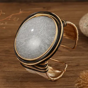 Primo piano del bracciale aperto largo con grande pietra di resina argentata e fili d'oro.