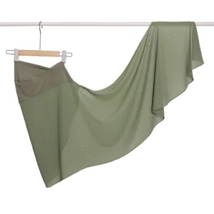 Dettaglio della sciarpa avvolgente in chiffon verde oliva con paillettes scintillanti e visiera morbida.