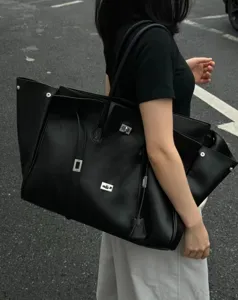 Large black leather tote bag with wing design and metal turn-lock, stylish commuter handbag.