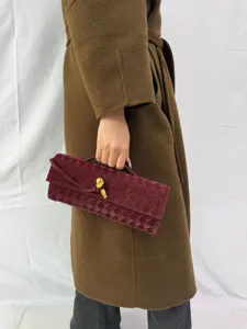 Detailed view of a luxury burgundy woven leather clutch bag with a gold metal knot lock.
