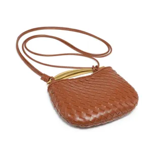 Kleine bruine geweven lederen crossbody tas met opvallend metalen handvat en smalle riem.