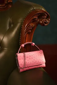 Close-up view of a chic pink ostrich pattern baguette shoulder bag with metallic chain and top handle.