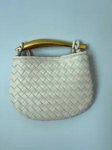 Gedetailleerde close-up van een geweven lederen handtas met een uniek gouden metalen handvat.