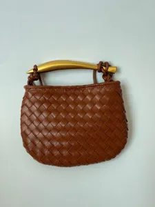 Detail van mini gevlochten lederen handtas met bruine textuur en luxe gouden handvat.