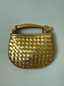 Gouden geweven lederen handtas detail met unieke sculpturale metalen handgreep en compacte vorm.