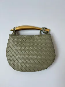 Detail van de geweven leren handtas met elegant gebogen metalen handvat voor stijlvol dagelijks gebruik.