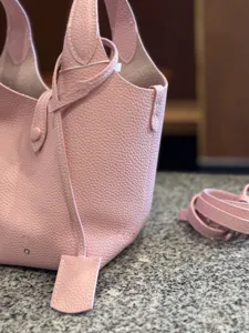Pink leather bucket bag detail showing soft lychee texture, top handles, and fine stitching.