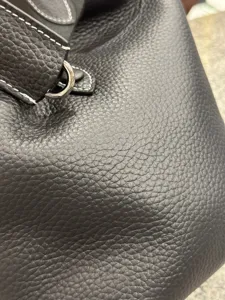 Black pebbled leather handbag detail shot featuring durable cowhide material and fine contrast stitching.