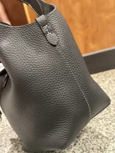 Close-up detail of dark grey pebbled leather bucket bag with contrast stitching texture.
