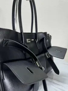 Black leather tote bag detail showing premium texture, dual top handles and metallic hardware.