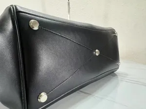 Black leather handbag bottom detail with metal feet and stitching. Premium commuter tote bag.