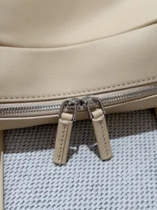 Close-up detail of beige leather boston bag zipper, showcasing premium texture and metal pullers.