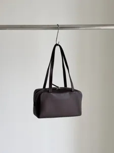 Detailed view of the dark brown leather bowling bag hanging gracefully on a metal hook.