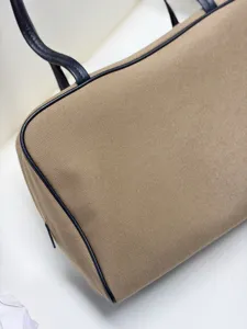 Close-up detail of khaki canvas handbag featuring dark leather piping and dual handles.